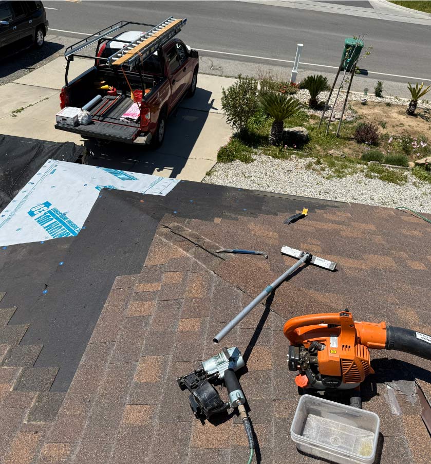 Roofing contractor tools including a pneumatic nail gun and titanium underlayment on a residential roof replacement project.