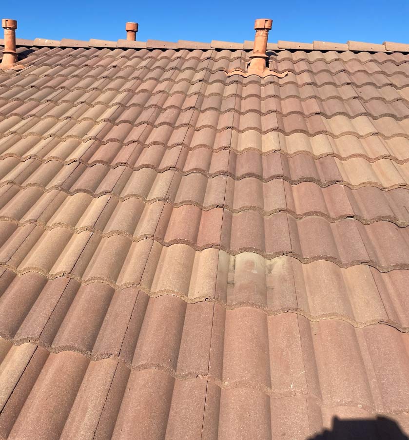 Close-up view of terracotta-colored concrete roof tiles and clay pipe vents on a residential home.